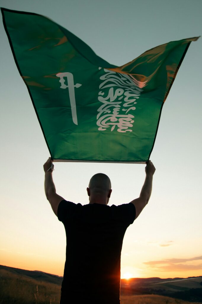 Man holding Saudi Arabia national flag waving in beautiful clouds.